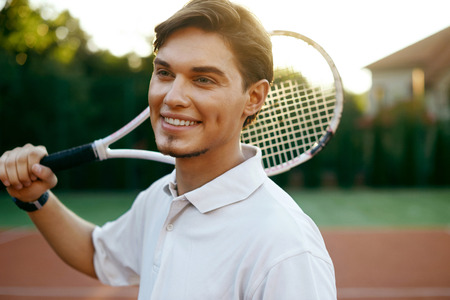 Sports Man Before Playing Tennis On Court. Portrait Of Young Attractive Male In White T-Shirt Holding Racket In Hands Outdoors. Active People. High Quality Image.の写真素材