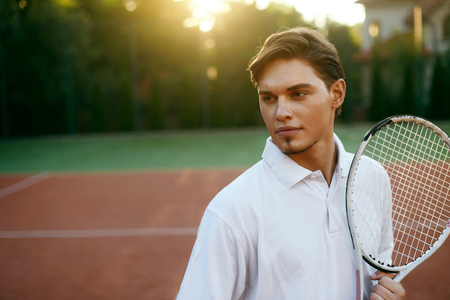 Sports Man Before Playing Tennis On Court. Portrait Of Young Attractive Male In White T-Shirt Holding Racket In Hands Outdoors. Active People. High Quality Image.の写真素材