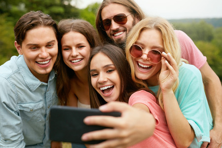 Happy Friends Taking Photos On Phone In Nature. Portrait Of Young Smiling People In Colorful Clothes Having Fun And Laughing On Weekend Outdoors. High Quality Image.の写真素材