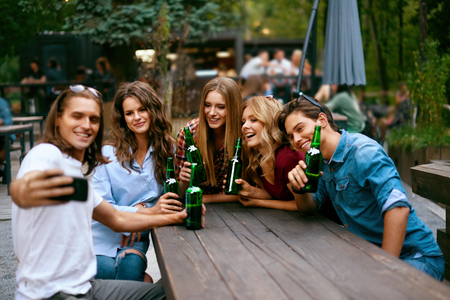 Group Of Friends Drinking Beer And Taking Photos On Phone. Happy Smiling Young People With Drinks In Hands Laughing And Spending Time Together On Summer Weekend. High Quality Image.の写真素材