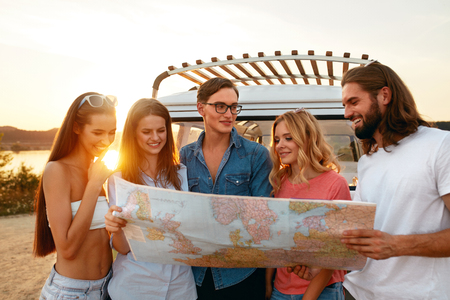 Summer Travel. Friends Using Map Near Car In Nature. Happy Smiling People Traveling In Bus On Weekend Vacation. Beautiful Young Men And Women Holding Map, Exploring Location On Trip. High Qualityの写真素材