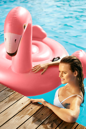 Summer Fashion. Beautiful Girl In Pool With Flamingo. Fashionable Happy Young Woman With Tanned...