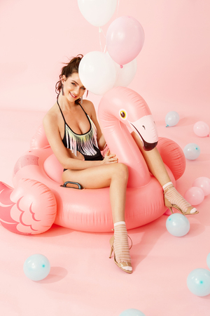 Summer Fashion. Woman Model In Swimsuit On Flamingo Having Fun Indoors. Beautiful Happy Young Female With Fit Body In Stylish Swimwear With Pink Inflatable Float And Colorful Balloons. High Resolutionの写真素材