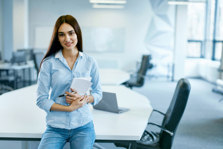 Woman In Office. Female At Work In Light Modern IT Office. Portrait Of Beautiful Smiling Young Worker In Casual Clothes With Arms Crossed At Workplace. Business Person, People At Work. High Qualityの写真素材
