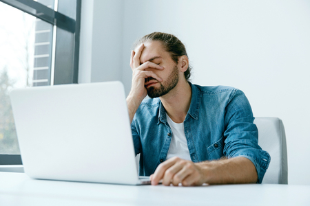 Work Stress. Man Working On Computer. Male Worker Feeling Stressed And Exhaused. Tired Man In Casual Clothes Sitting At Workplace With Laptop In Modern Office. Failure And Hard Work. High Qualityの写真素材