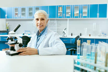 Laboratory. Female Scientist Working In Light Laboratory. Portrait Of Happy Smiling Mature Woman Doctor In White Coat Sitting With Microscope At Workplace In Medical Laboratory. High Resolution.の写真素材