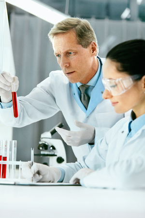 Laboratory Research. Scientists Doing Blood Analysis. Portrait Of Young Female And Male Doctors In Lab Coats Holding Test Tube With Blood Sample, Doing Medical Test. Clinical Laboratory. High Qualityの写真素材