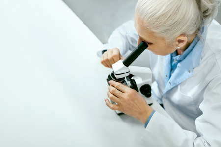 Laboratory Research. Female Scientist Using Microscope. Portrait Of Mature Woman In White Coat Working At Workplace In Modern Light Laboratory. Clinical Laboratory. High Quality Imageの写真素材