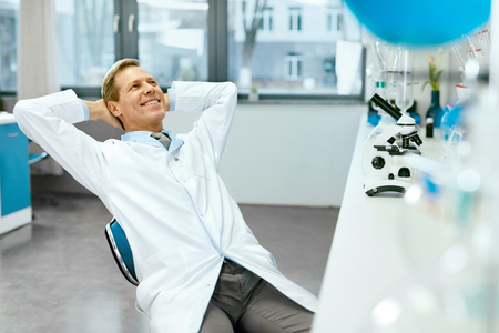 Male Scientist In Laboratory Portrait. Happy Handsome Smiling Mature Man In White Laboratory Coat Holding Relaxing At Workplace In Modern Scientific Laboratory. High Quality Image.の写真素材