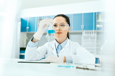 Scientific Laboratory. Female Scientist With Laboratory Glass. Portrait Of Beautiful Woman In Glasses Holding Glassware With Liquid In Hand, Looking At Chemical Reaction At Workplace. High Resolution.の写真素材