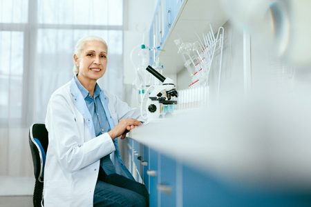 Laboratory. Female Scientist Working In Light Laboratory. Portrait Of Happy Smiling Mature Woman Doctor In White Coat Sitting With Microscope At Workplace In Medical Laboratory. High Resolution.の写真素材