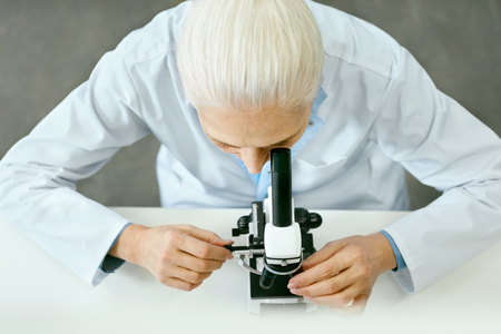 Laboratory Research. Female Scientist Using Microscope. Portrait Of Mature Woman In White Coat Working At Workplace In Modern Light Laboratory. Clinical Laboratory. High Quality Imageの写真素材