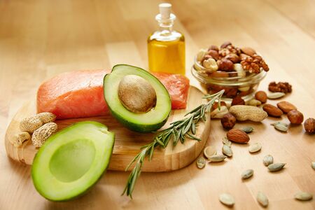 Healthy Food. Ingredients Full of Healthy Fat On Table. Close Up Of Fresh Organic Avocado And Olives, Nuts And Seeds, Olive Oil And Salmon Fillet Lying On Wooden Background In Kitchen. High Qualityの写真素材