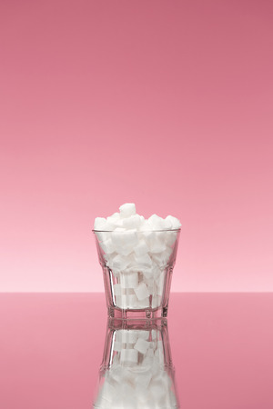 Sugar In Drinks. Glass Full Of White Sugar Cubes. Close Up Of Transparent Glass With Refined Sugar On Pink Background. High Qualityの写真素材
