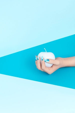 Blue Nails And Apple In Hand On Geometric Turquoise Background. Close Up Of Stylish Blue Manicure And Colored Fruit In Hand. Nail Designs. High Qualityの写真素材
