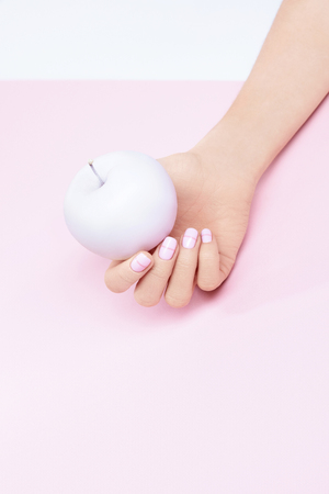 Woman Hand With Pink Pastel Nails And Apple. Close Up Of Stylish Geometric Pastel Manicure And Fruit In Hand On Light Background. Nail Designs. High Quality Image.の写真素材