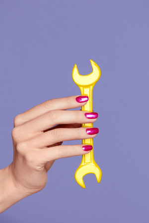 Fashion Nail Art. Pink Nails On Purple Background Holding Instrument. Close Up Of Woman Hands With Bright Nail And Soft Smooth Skin Holding Colorful Wrench. High Quality Image.の写真素材
