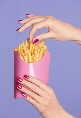 Pink Nails. Female Hands And Fries On Violet Background. Close Up Of Female With Colorful Manicure On Hands Holding Pink French Fries. Nail Art. High Quality Image.の写真素材