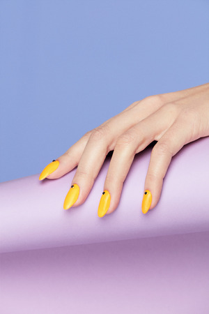 Nails Design. Hands With Bright Yellow Manicure On Violet Background. Close Up Of Female Hands With Trendy Orange Nails On Purple Background. Art Nail. High Quality Image.の写真素材