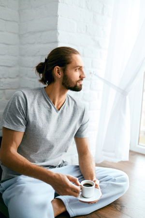 Man Drinking Coffee At Home In Morning. Young Male Holding Cup Of Hot Beverage, Enjoying Morning. High Resolution.の写真素材