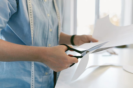 Tailor Cutting Sewing Pattern With Scissors. Close Up Of Female Hands Cutting Paper Patterns In...