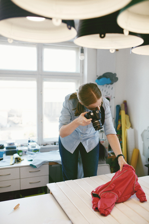 Woman Taking Photos Of Dog Clothes In Clothing Atelier. Female Fashion Designer Taking Pictures Of Red Overall For Pet On Camera At Her Workshop の写真素材