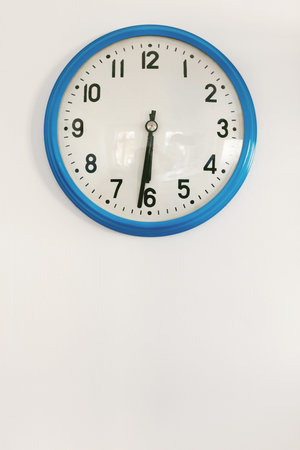 Close Up Of Blue Clock Hanging On White Wall Showing Half Past Six