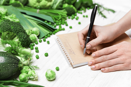 Diet Plan. Female Hand Writing In Notebook Near Fresh Green Vegetables On White Table. High Resolution.の写真素材