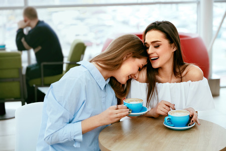 Girls Friends Drinking Coffee In Cafe, Speaking And Laughing While Sitting At Table In Shopping Mall. High Resolution.の写真素材