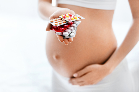 Pregnancy Vitamins And Medications. Close Up Of Pregnant Woman Holding Pills In Hand Near Belly. High Resolutionの写真素材