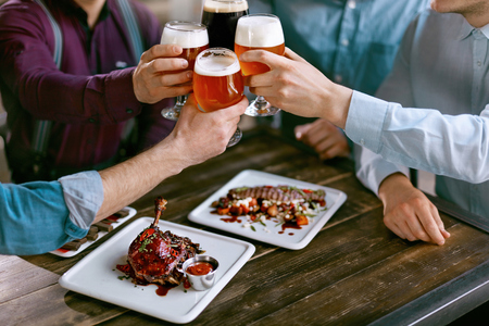 Drinking Beer. Friends Raising Glasses Of Beer At Table With Food In Pub Bar. High Resolution.の写真素材