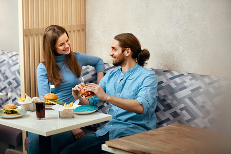 Couple With Burgers. Man And Woman Eating Fast Food In Cafe. High Resolution.の写真素材