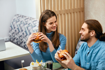 Couple With Burgers. Man And Woman Eating Fast Food In Cafe. High Resolution.の写真素材