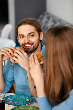 People Having Dinner, Eating Burgers At Cafe. Friends Eating Fast Food In Restaurant. High Resolution.の写真素材