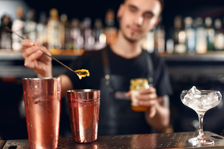 Cocktail Bar. Bartender Making Cocktails At Bar Counter. Barman Preparing Drink, Pouring Spoon Of Honey In Shaker. High Resolutionの写真素材