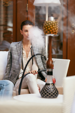 Woman Smoking Shisha In Hookah Bar. Beautiful Fashionable Girl Smoke Fruit Cup Hookah At Luxury Lounge Restaurant. High Resolutionの写真素材