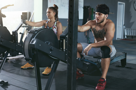 Gym. Man And Woman Training On Rowing Machine At Crossfit Clubの写真素材