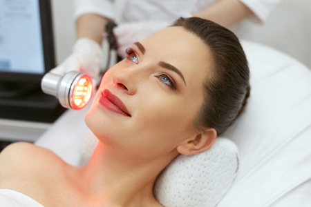 Cosmetology. Woman On Facial LED Red Light Therapy At Clinic. Cosmetologist Using Red Light For Skin Treatment. High Resolution