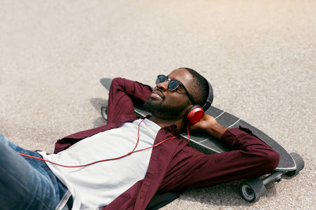 Man Listening Music In Headphones On Street, Relaxing On Longboard. High Resolution