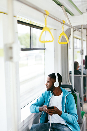 Man Riding Bus, Listening Music With Headphones And Phone In Public Transport. Handsome African Male With Earphones. High Resolutionの写真素材