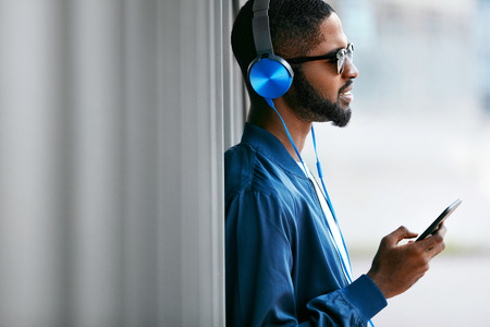 Listen Music. Man With Headphones And Phone In Fashion Clothes. Handsome Black Male Listening Music Outdoors. High Resolutionの写真素材
