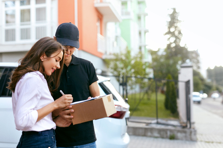 Delivery Courier. Man Delivering Package To Woman. Client Signing Delivery Documents. High Resolutionの写真素材