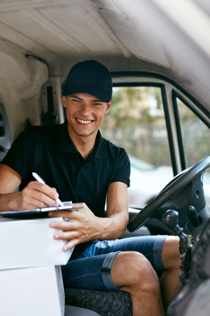 Delivery Courier In Car With Boxes. Man Delivering Packaging, Filling Delivery Document. High Resolutionの写真素材