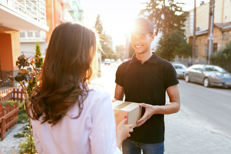 Courier Delivering Package To Woman. Client Receiving Box From Delivery Man Near Home Outdoors. High Resolutionの写真素材