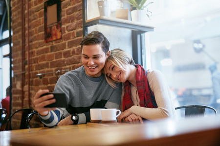 Couple Using Phone In Cafe For Video Calling Or Taking Photos. Happy Young People With Smartphone In Coffee Place. High Resolutionの写真素材