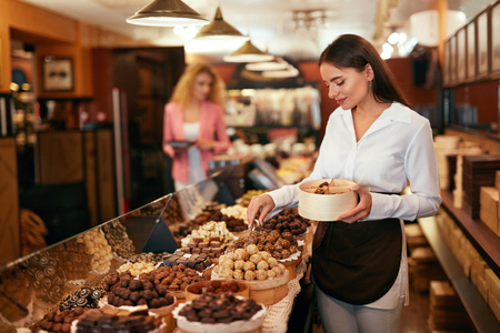 Chocolate Store. Woman Working In Chocolate Shop. Female Worker Picking Candies In Gift Box. High Resolutionの写真素材