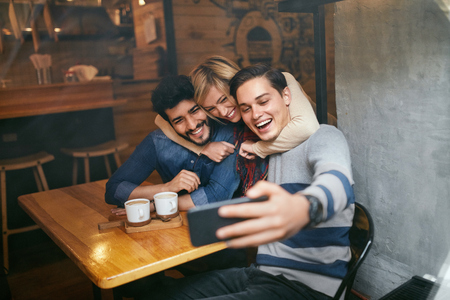 Friends Taking Photos On Phone In Cafe. Happy People Making Video Call, Having Fun Together. High Resolutionの写真素材