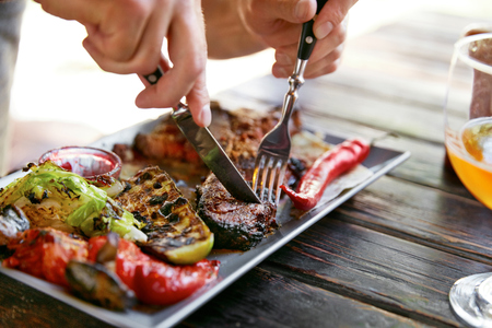 Eating Food. Close Up Man Eating Steak With Vegetables In Restaurant. Male Hands Cutting Grilled Meat With Knife And Fork. High Resolutionの写真素材