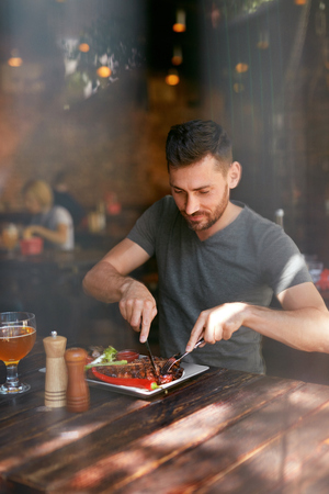 Restaurant. Man Eating Food With Beer At Cafe. Male Eats Barbecue Steak With Grill Vegetables. High Resolutionの写真素材