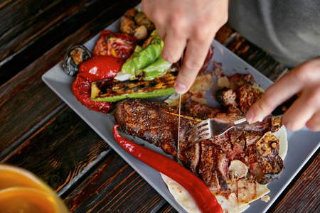 Eating Food. Close Up Man Eating Steak With Vegetables In Restaurant. Male Hands Cutting Grilled Meat With Knife And Fork. High Resolutionの写真素材